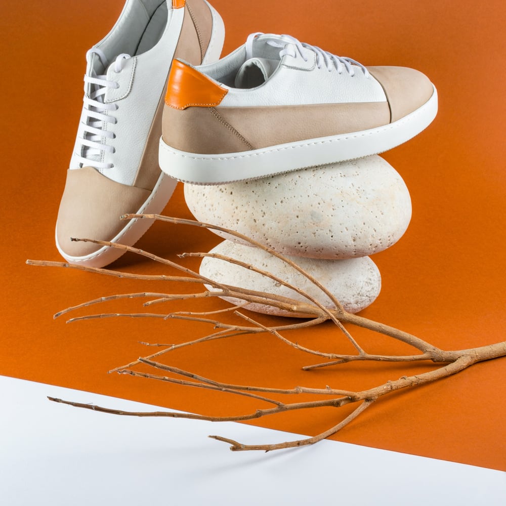 Fashionable white sneakers with orange accents on a rock.